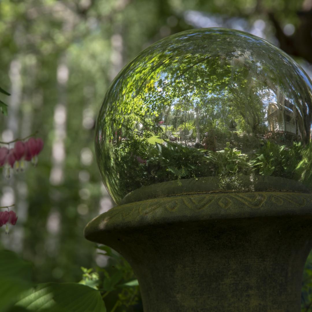 Käpälämäen pihaa. kuvassa lasipallo-pihakoriste, josta heijastuu ympäröivää vehreää vanhaa puutarhaa.
