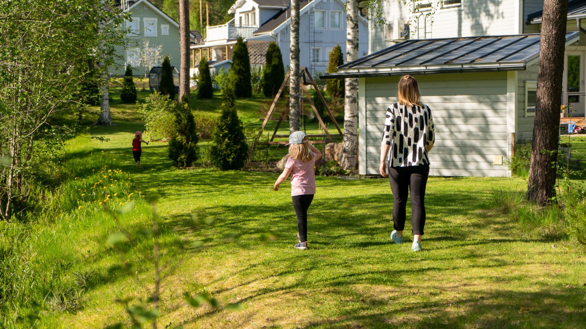 Kaisa ja tyttäret kävelevät nurmikolla omakotitalonsa takapihalla.