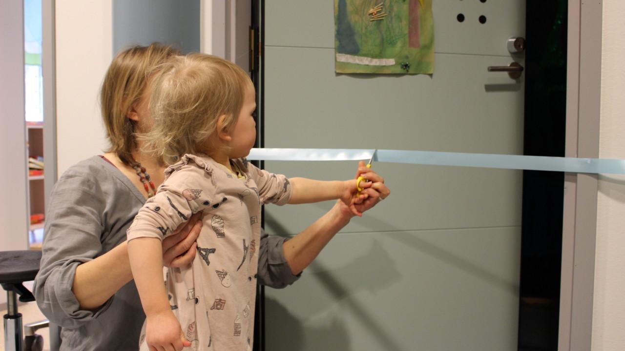 Lapsi leikkaa nauhaa Orivarsan päiväkodin näyttelyn avajaisissa.