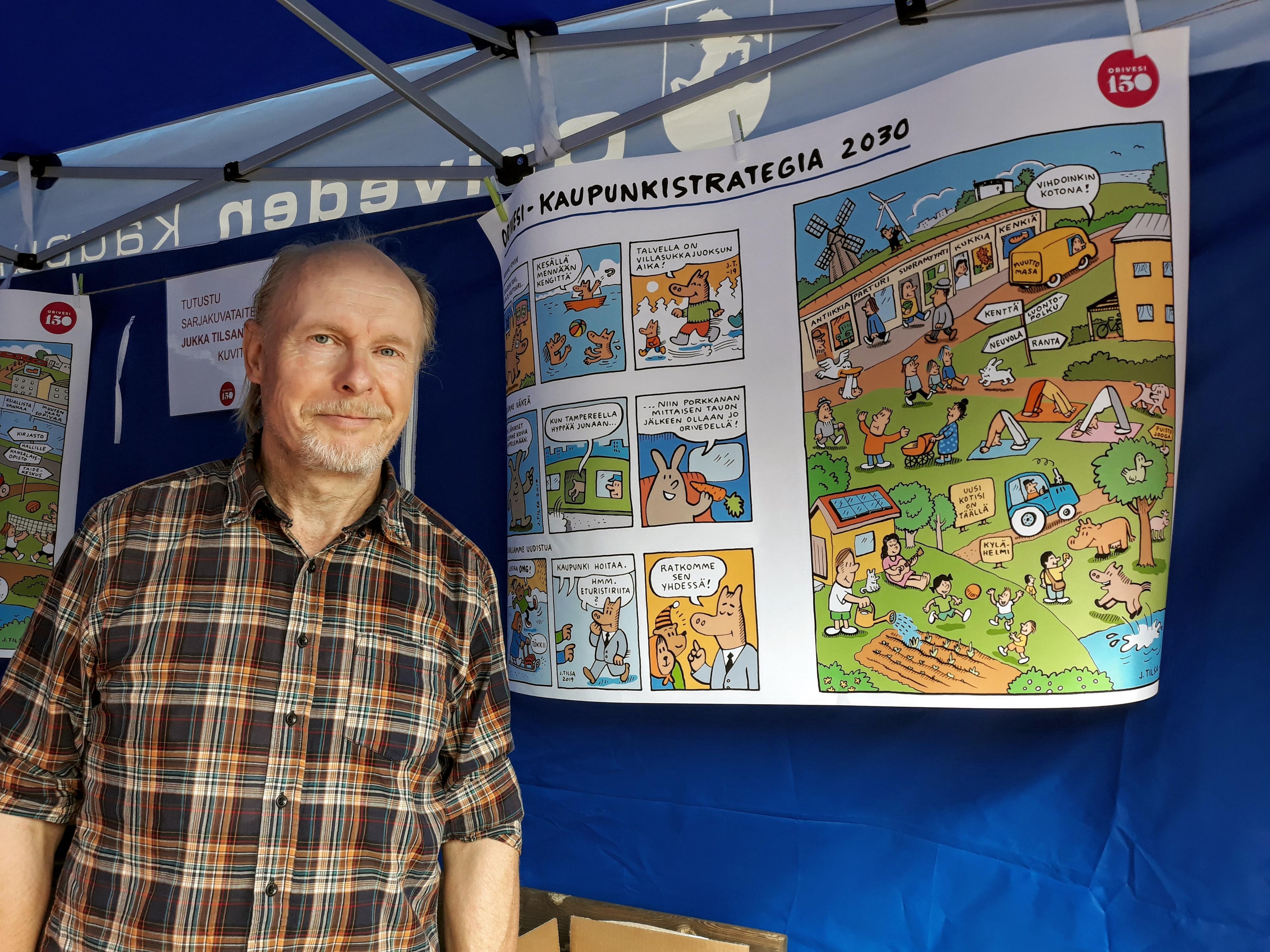 Sarjakuvataiteilija Jukka Tilsa piirtämänsä kaupunkistrategian sarjakuvakuvituksen vieressä.