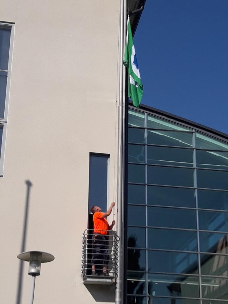Tilapalvelun työntekijä nostaa Vihreän lipun Orivesi-talon lipputankoon.