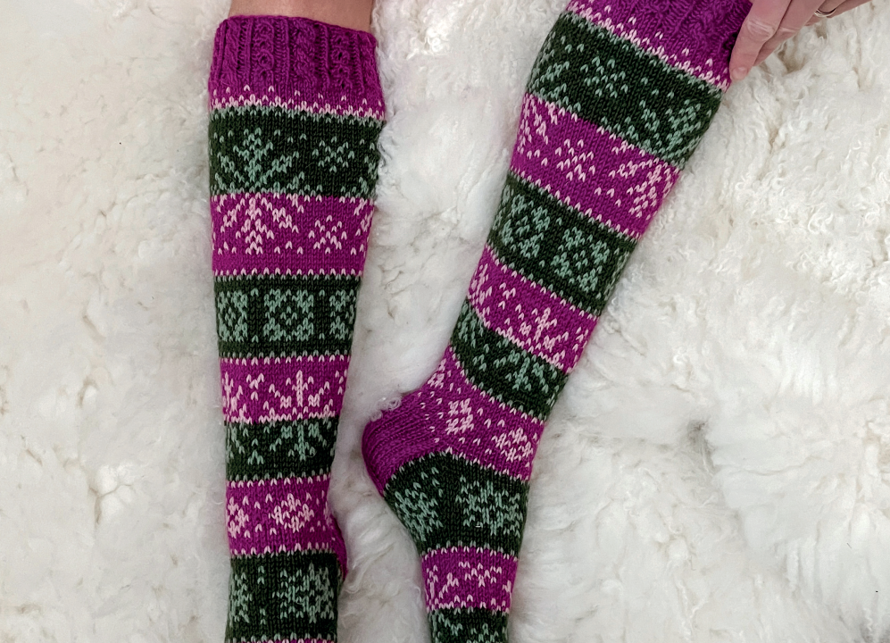 Henkilön jalat, joissa on violetin ja vihreän väriset, kuviolliset Novitan Talvetar-sukat.