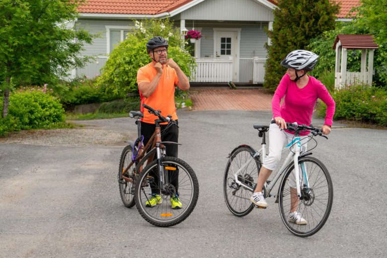 Eläkeläispariskunta kotinsa edustalla lähdössä pyöräilemään.