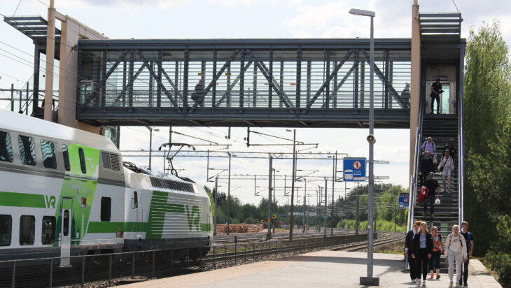 Juna seisahtuneena Oriveden rautatieasemalle, junamatkustajia laskeutumassa alas ylikulkukäytävältä.