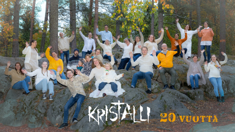 Kristalli-kuoro kuvattuna ulkona kallioisella rinteellä, kuvan päällä kuoron logo ja teksti 20v.